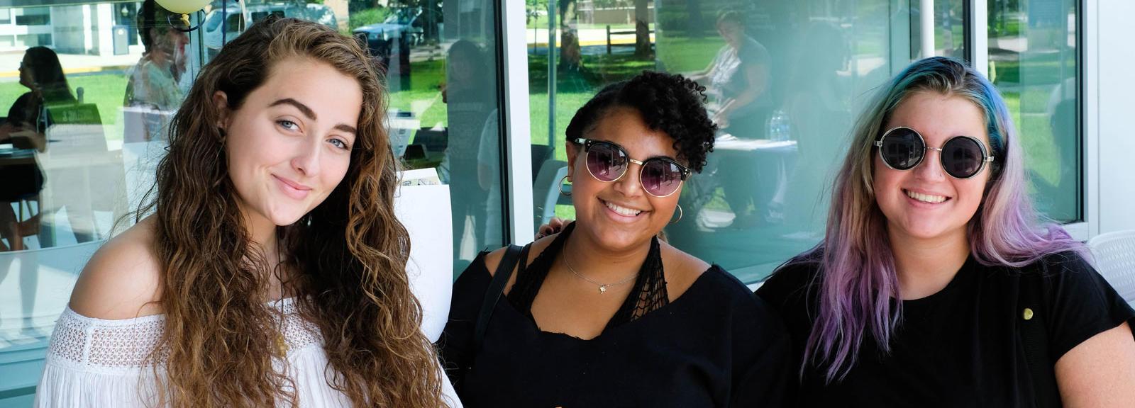 three girls smiling in front of student center